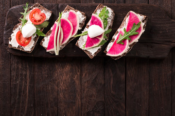 Sandwiches with cream cheese and fresh cucumber, radish,tomatoes,arugula and mozzarella. Fresh healthy appetizer snack with crispbread.