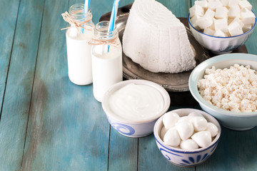 tasty healthy dairy products on a table on a blue background: sour cream, cottage cheese, mozzarella cheese, butter,ricotta and milk in a bottle
