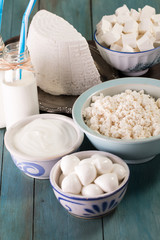 tasty healthy dairy products on a table on a blue background: sour cream, cottage cheese, mozzarella cheese, butter,ricotta and milk in a bottle