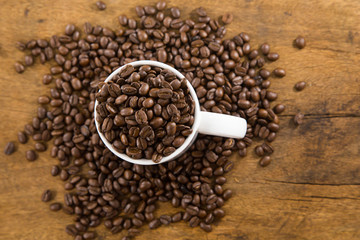 White cup full of coffee beans on Roasted Coffee Beans and wood background, top view.jpg