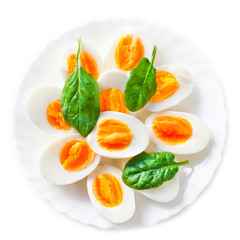 Boiled halved eggs on plate decorated with spinach leaves isolated on white. Healthy salad..