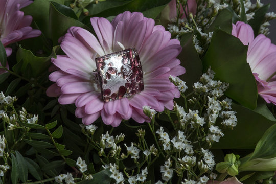 One beautiful pink glass ring on the fresh flower and green leaves as background