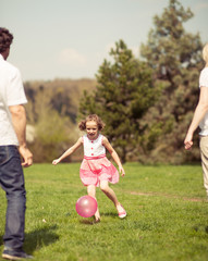 Daughter kicking ball to father and mother in park
