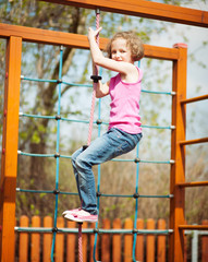 Obraz premium Young girl climbing rope in playground