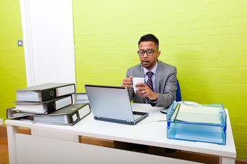 Portrait of Indian Businessman holding mug and working on his laptop computer at his desk