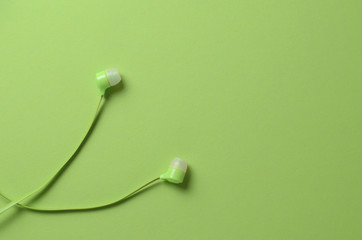 Bright green headphones for the player on a similar green background. Monochrome concept photo for website design, postcards, advertising.
