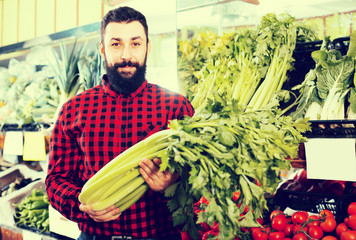 Adult male seller offering celery in shop