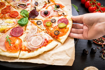 Pizza with ingredients and woman hand on dark background. Food background. Flat lay, top view.