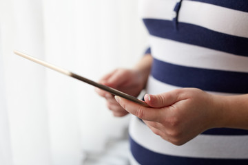 Close up of pregnant woman using tablet computer near a window