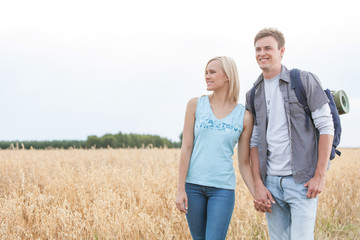 Young hiking couple holding hands while standing on field