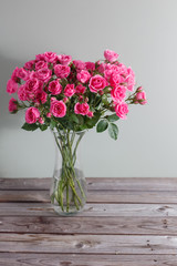 branchs of pink roses in a vase on wooden table