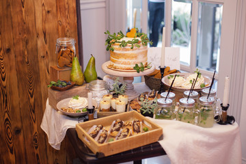 sweet bar with eclairs, lemonade,sweets and white cake  decorated with greenery in area of wedding party