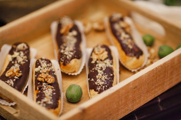 Eclairs with chocolate and walnut on wooden tray. Sweet bar in area of wedding party