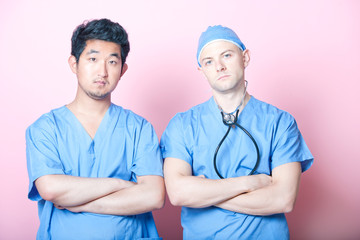 Portrait of two male surgeons standing with arms crossed over pink background