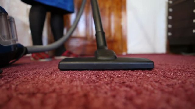A woman in a blue robe vacuuming a red carpet
