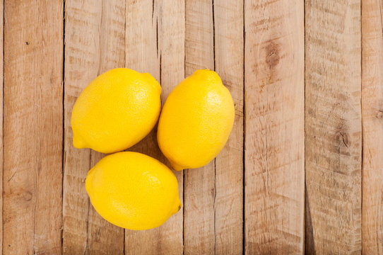 Three fresh yellow lemons on wooden desk background