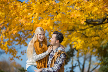 Fototapeta premium Portrait of happy woman sitting on man's lap in park during autumn