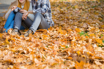 Low section of couple with camera sitting on autumn leaves in park