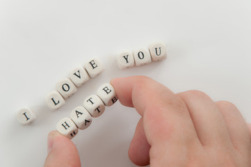 Man hand with word HATE spelled by dice between fingers over phrase I love you