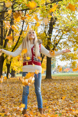 Autumn leaves falling on young woman with arms outstretched in park