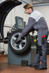 Side view of male mechanic repairing car's wheel in workshop