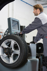Obraz na płótnie Canvas Side view of mid adult male mechanic repairing car's wheel in workshop