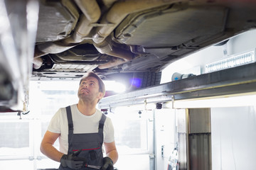 Mid adult male automobile mechanic worker examining car in workshop