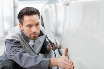 Young automobile mechanic examining car in repair store
