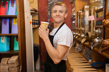 Portrait of male salesperson holding disposable coffee cup in store