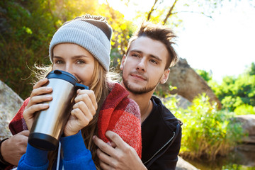 Young couple sitting on rock in canyon, smiling, drinking tea.