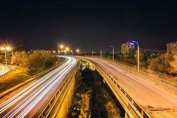 Fototapeta na wymiar Bridge, curve road, night city landscape, freezelight car lights, long exposure,