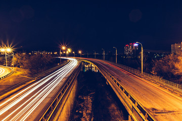 Fototapeta na wymiar Bridge, curve road, night city landscape, freezelight car lights, long exposure,