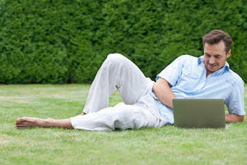 Obraz premium Full length of young man using laptop while lying on grass in park