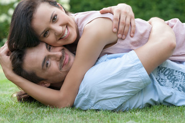 Portrait of smiling young couple embracing while lying in park