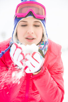 Young woman wearing winter coat blowing snow outdoors