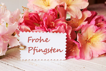 Rhododendron-Blüten auf weißem Holztisch mit Schildchen Frohe Pfingsten