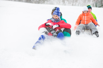 Fototapeta na wymiar Young couples enjoying sled ride on snow covered slope