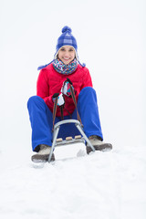 Full length portrait of happy young woman enjoying sled ride in snow