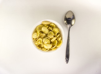 Bowl of yellow corn flakes with spoon on white background