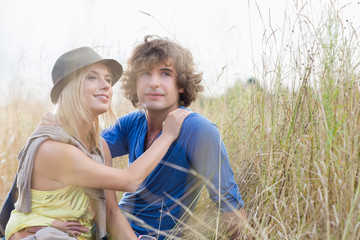 Loving young couple looking away while sitting in field