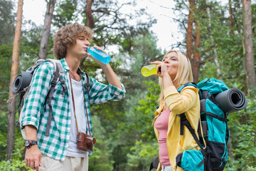 Fototapeta premium Young hiking couple drinking energy drinks in forest