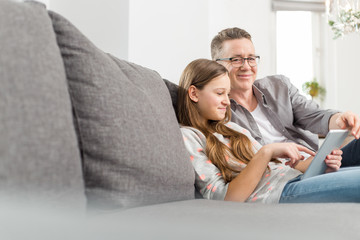 Portrait of smiling father assisting daughter in using digital tablet on sofa at home