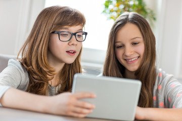 Sisters using digital tablet at table in house