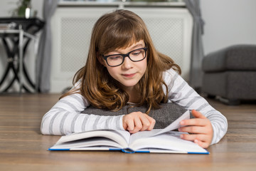 Teenage girl reading book while lying on floor at home