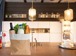 Shopping for cooking, healthy eating. Paper bag with delivered food products - milk, bread, green salad, wine on kitchen table. Kitchen background. Concept of shopping, cooking, eating. Copy space