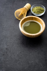Matcha green tea in a bowl and bamboo whisk on black slate
