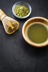 Matcha green tea in a bowl and bamboo whisk on black slate.Copyspace
