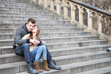 Fototapeta na wymiar Full length of loving woman kissing man while sitting on steps outdoors
