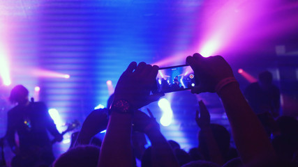 Fototapeta na wymiar Fans waving their hands recording video and taking pictures with smart phones at music concert. People crowd partying at rock concert in night club.