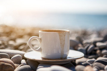 A cup of spilled coffee stands on stones near the sea shore